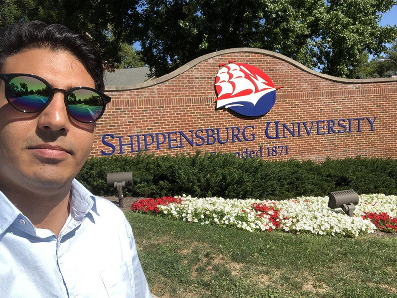 Abolfazl Farajnezam wearing sunglasses and taking a selfie in front of Shippenburg University entrance sign
