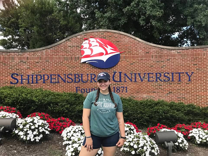 Lacey Carey posing in front of Shippensburg University front entrance to campus