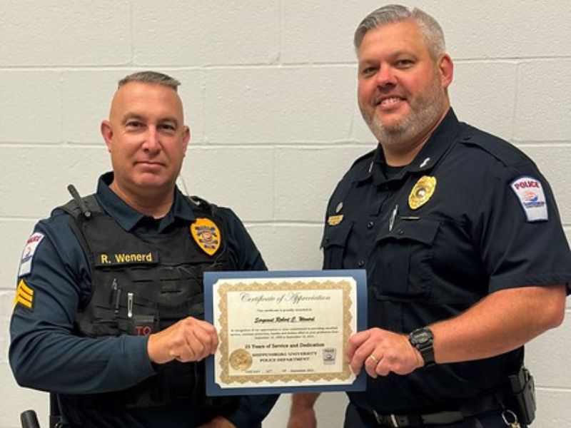 Two Shippensburg University police officers standing together and smiling, each with a hand on a certificate they are presenting between them